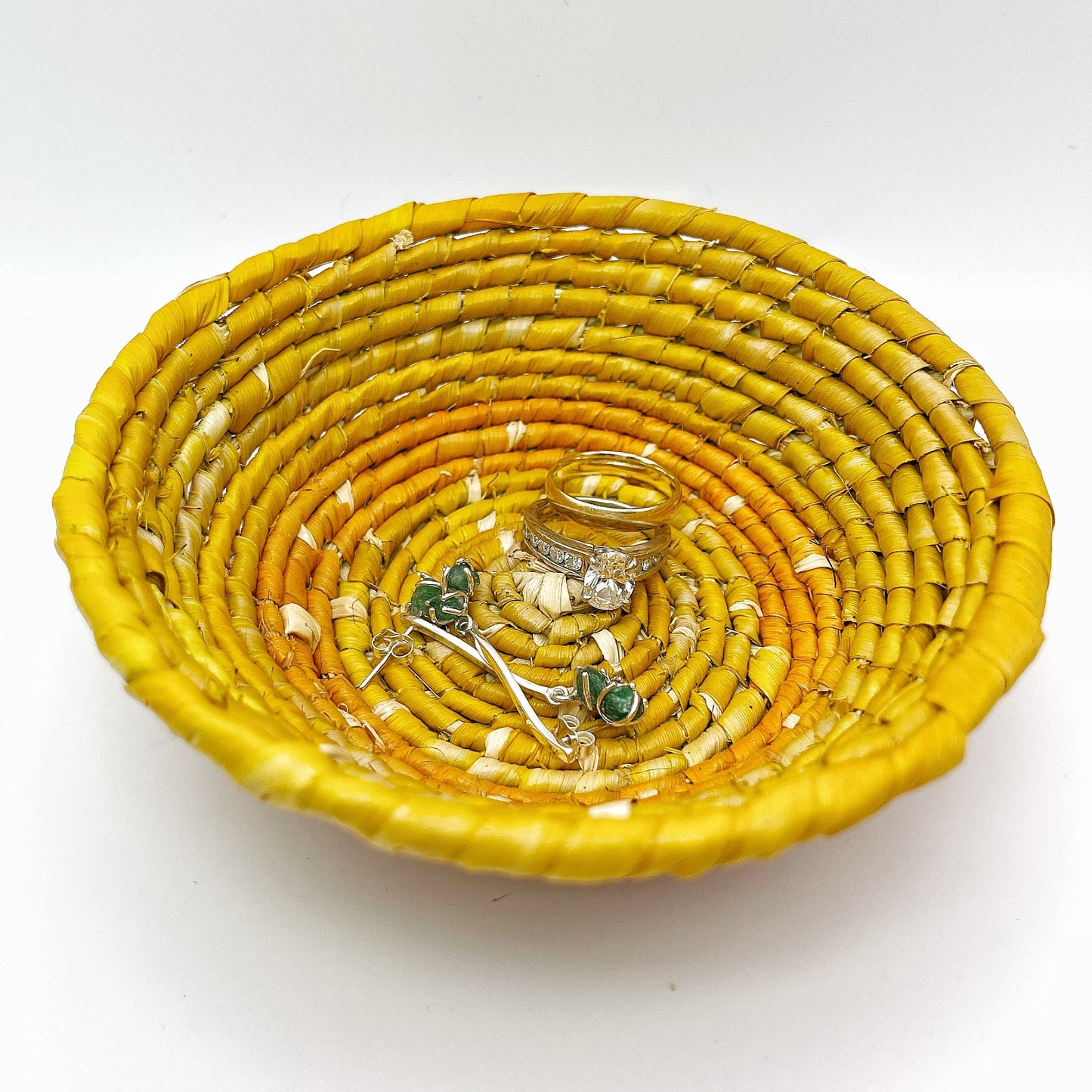 The bowl features a beige center with spiraling patterns in shades of yellow and a bold orange edge, holding earrings and rings, demonstrating its use for small items.
