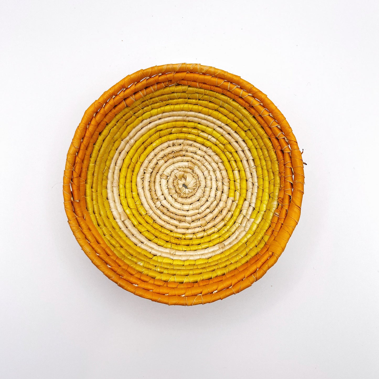 This trinket bowl features a gradient from a natural beige center to bands of yellow, and a bold orange rim, all in a spiraling woven pattern.