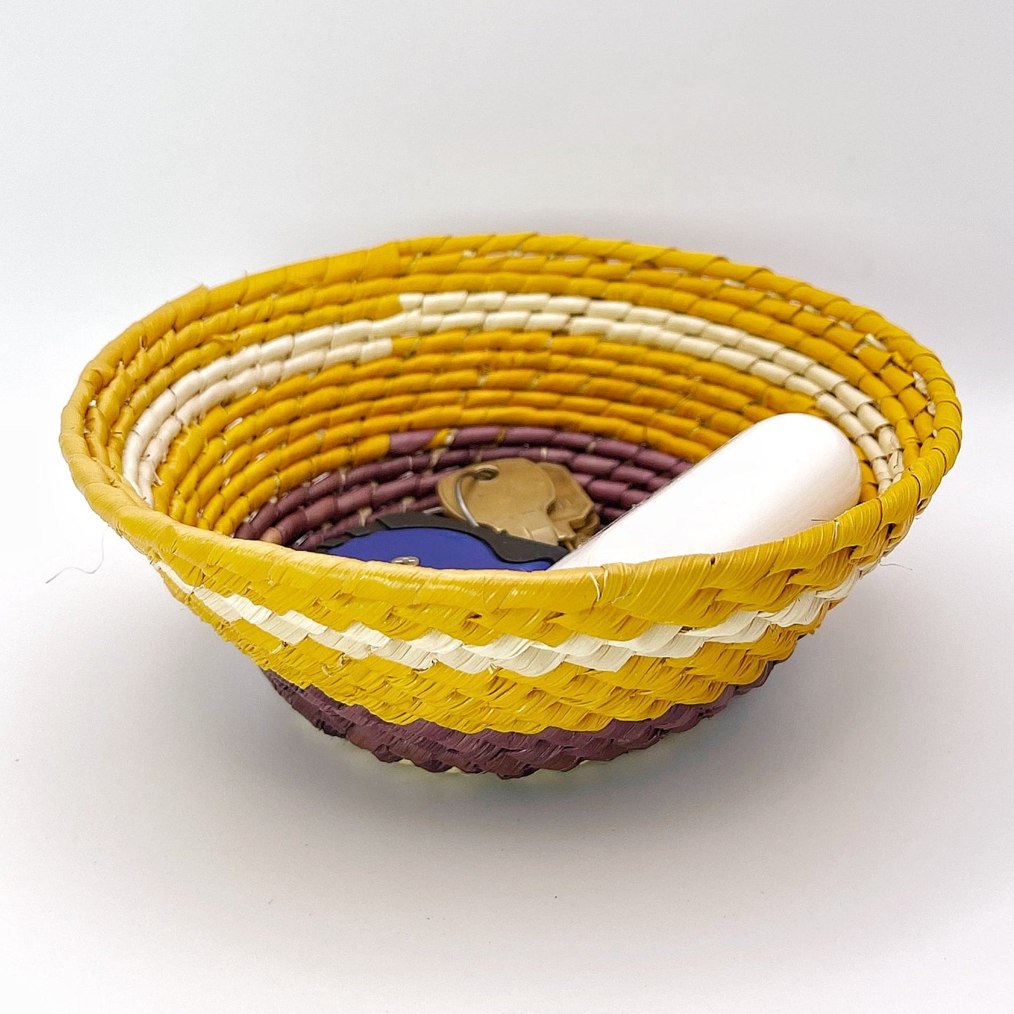 The bowl has layers of white, mustard yellow, burgundy, and deep yellow, with items inside demonstrating its utility for holding small objects like keys.