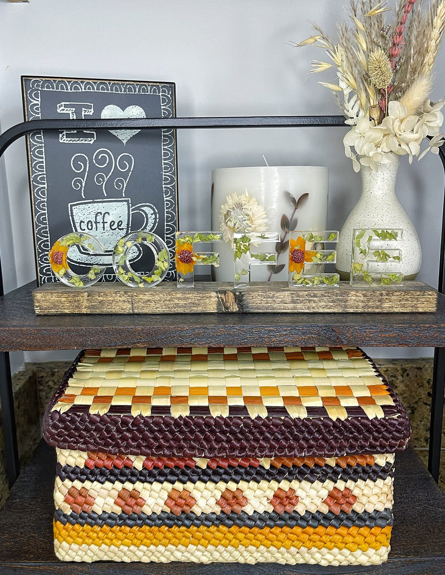 A handwoven tucuma palm box in a beautiful array of burgundy, brown, black, beige, and yellow stripes, creating an intricate pattern atop a modern shelf