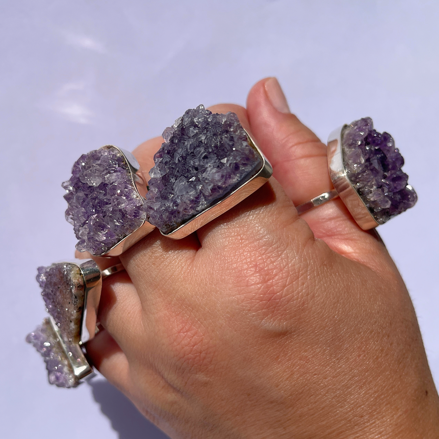 A hand showcasing five stunning raw amethyst rings, one on each finger.