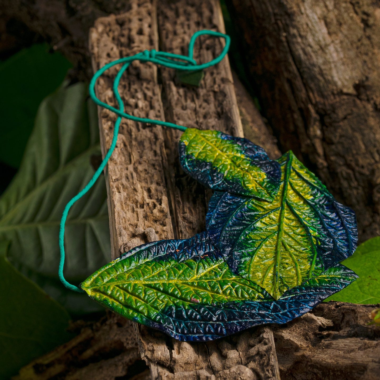 Realistic leaf necklace handcrafted from natural rubber & açaí seed fibers. Blue-green hues mimic nature's beauty, suspended on a turquoise cord for a striking contrast.