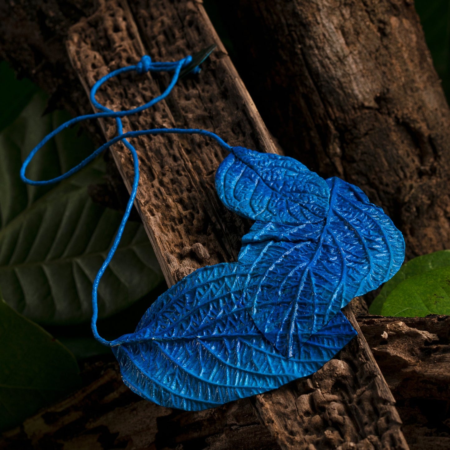 Two-toned blue leaf necklace! Handcrafted from natural rubber & açaí fibers, it transitions from dark to vibrant blue with textured veins. A blue cord suspends this eco-friendly piece.