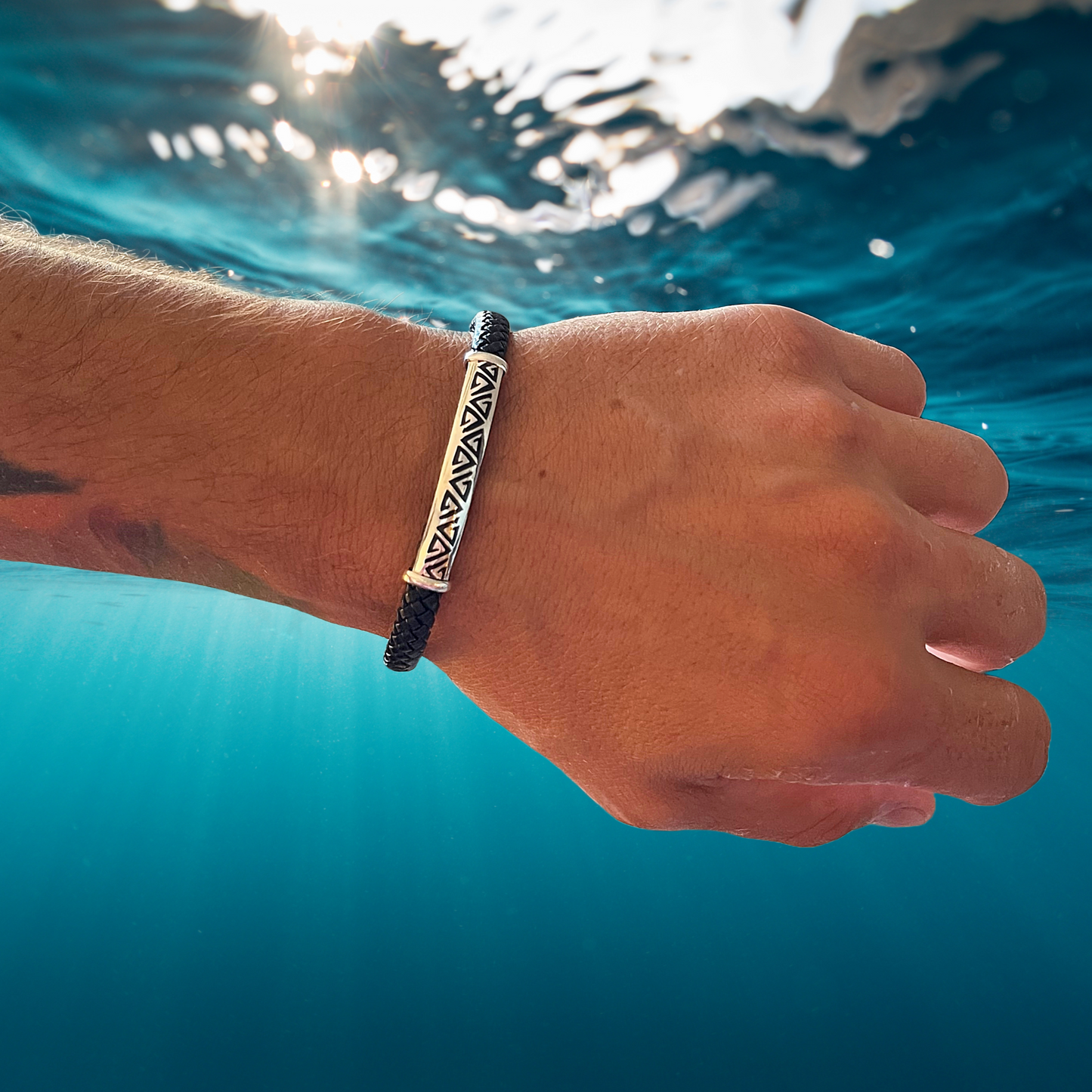 A hand on water showcases a .950 silver bracelet with a triangular pattern, symbolizing nature's connection on a vegan leather band.