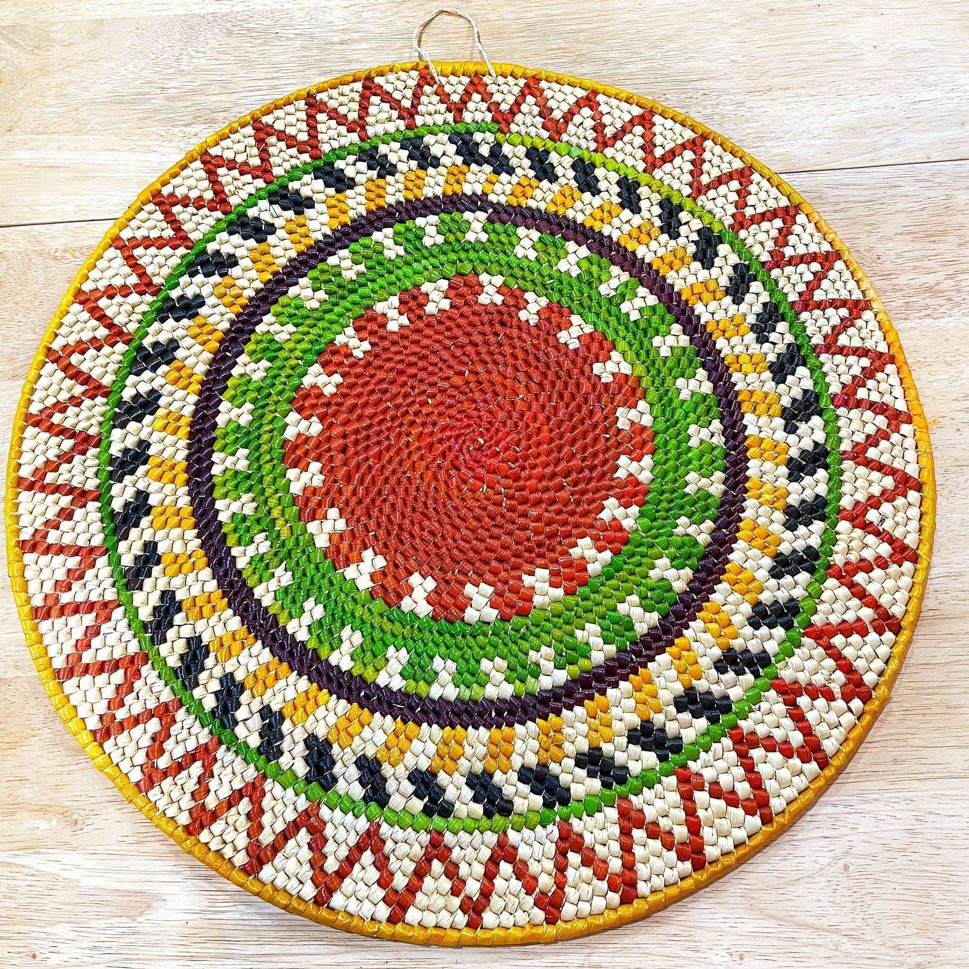 Handwoven Tucumã palm mandala wall art from the Amazon. Sunburst pattern features shades of green, red, yellow, orange, blue, purple, and cream.  Symbolizes positive energy and new beginnings.  Made by artisans using traditional techniques. 