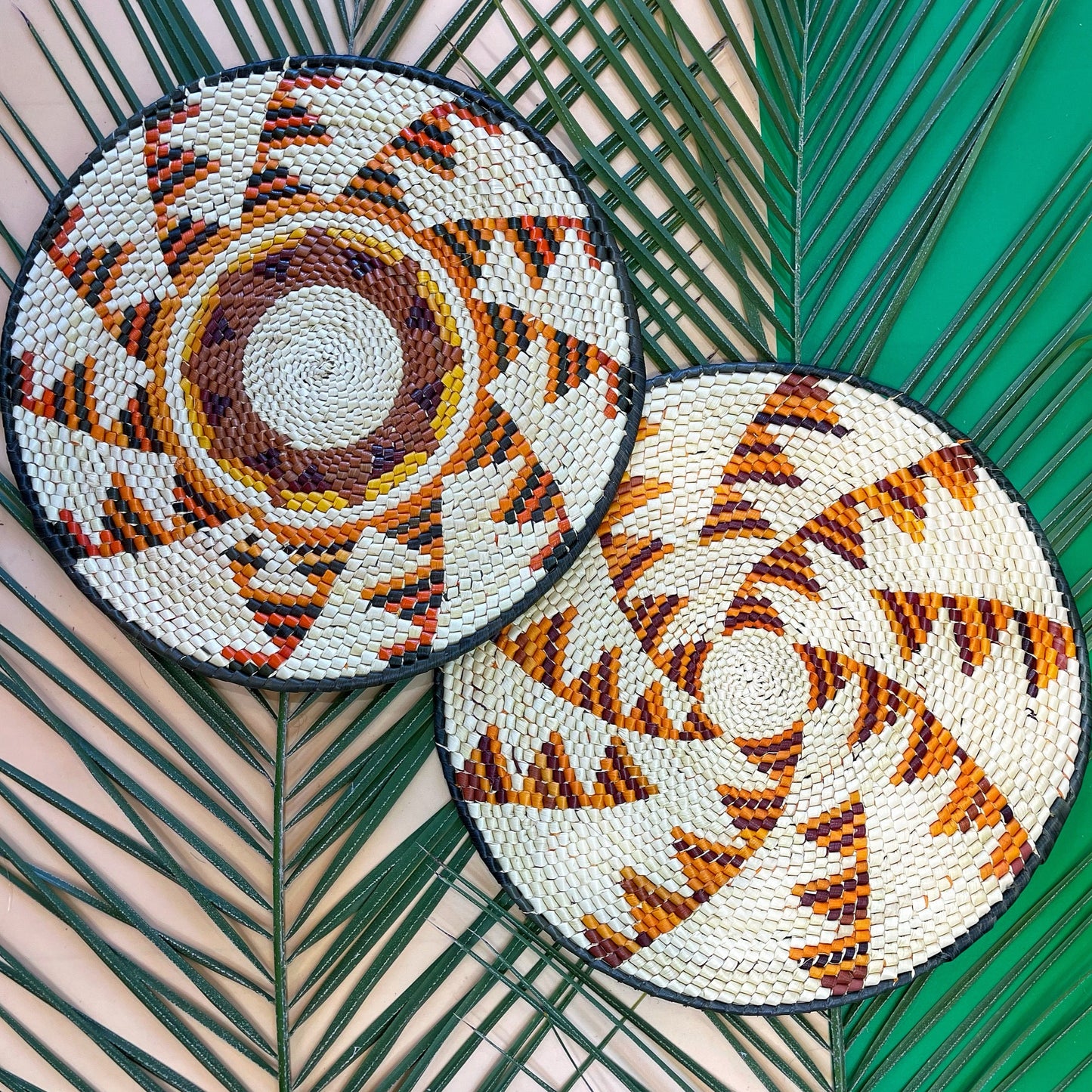 Round placemat from tucuma palm fibers in shades of brown, beige, orange, yellow and black. The center features a geometric design with concentric circles and radiating lines.