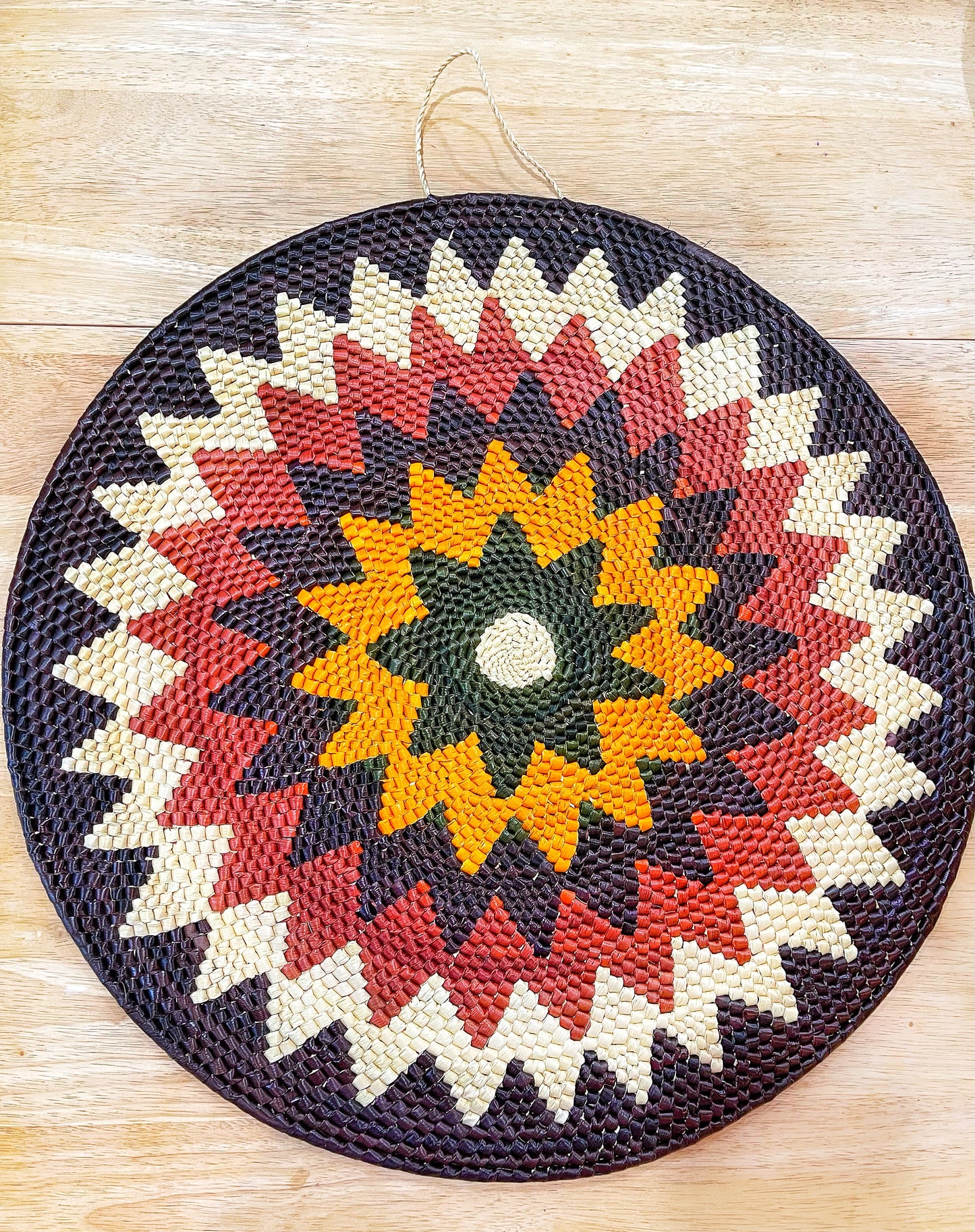 A handwoven Amazon mandala wall hanging, featuring a kaleidoscopic pattern with a central beige circle, radiating layers of green, yellow, red, and purple. It's a vibrant display of artisan skill and cultural heritage