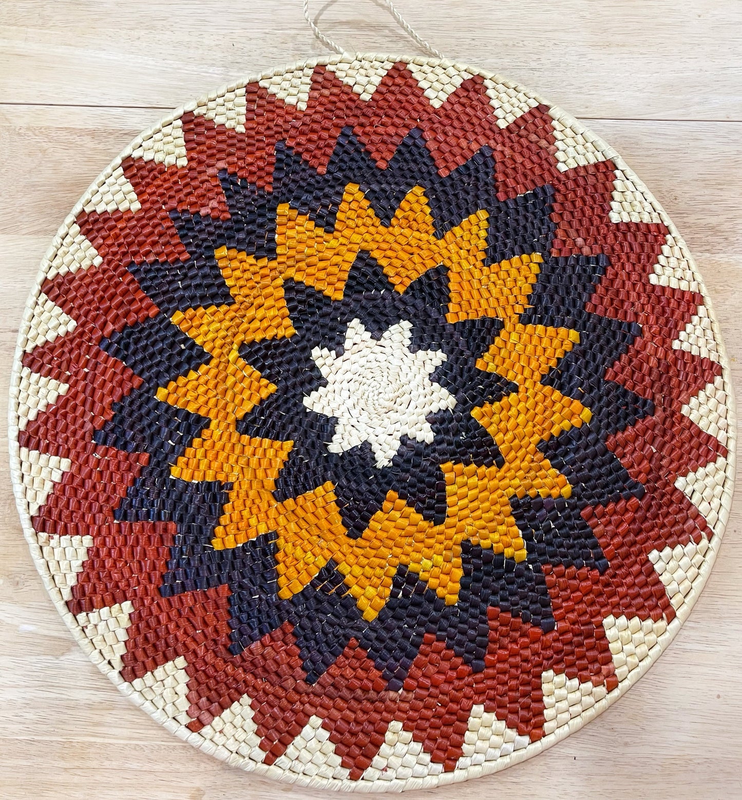 Vibrant handwoven Tucuma palm mandala wall art. Sunburst pattern in red, orange, blue/purple, & cream adds Amazonian flair.