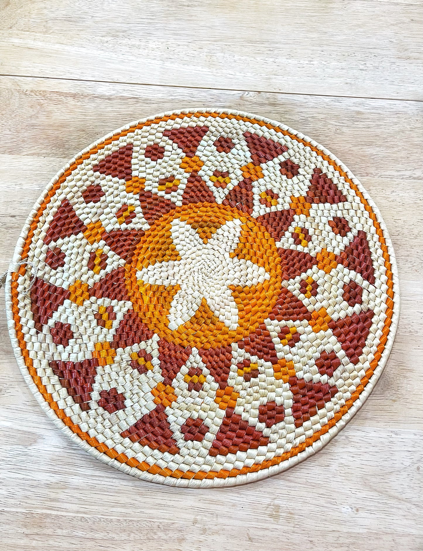 This handcrafted mandala wall hanging boasts a star-like central motif encircled by floral patterns in shades of cream, orange, and deep rust, set against a rich, earthy background.