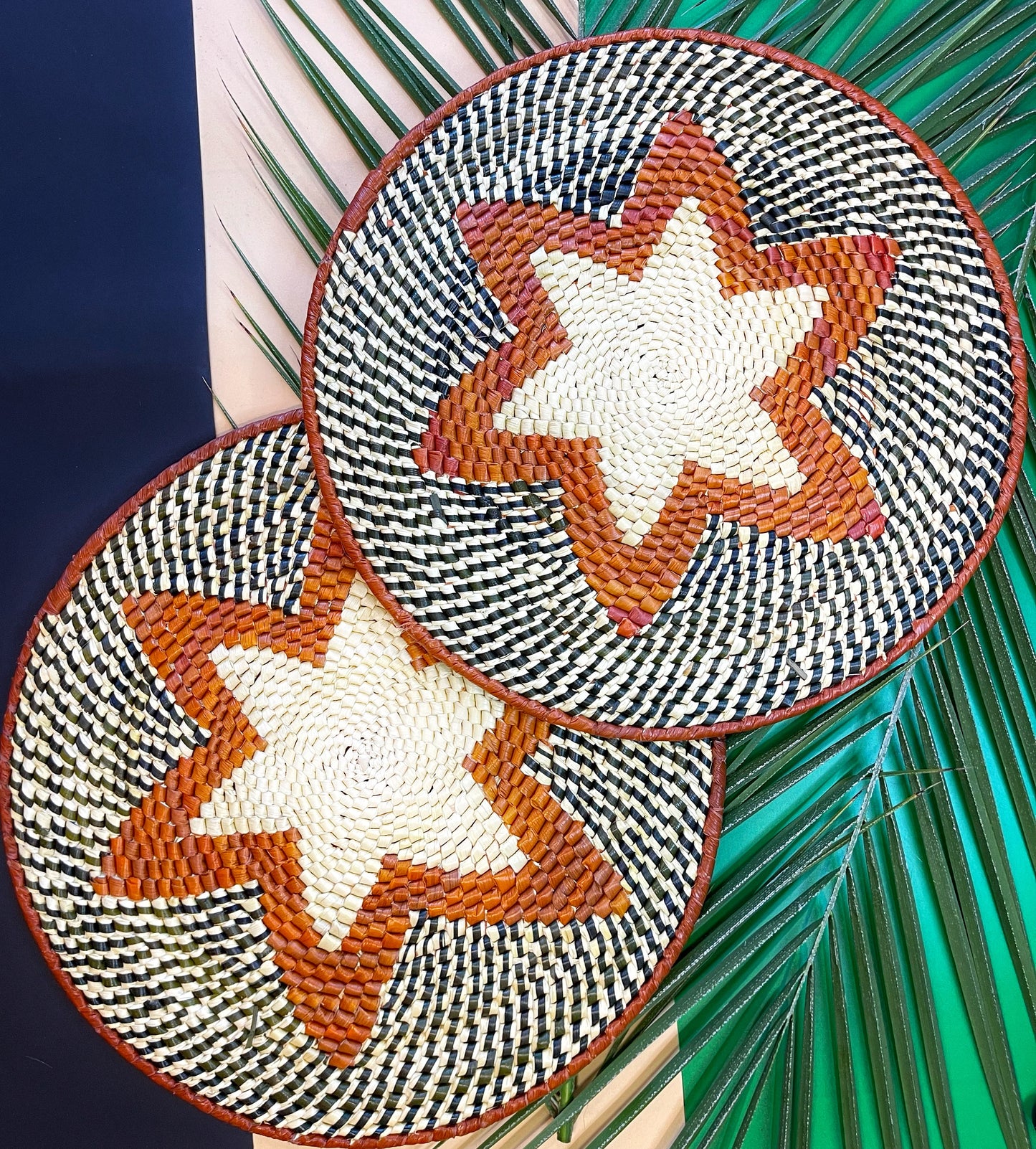 Round placemat handwoven from tucuma palm fibers in shades of brown and black. Features a geometric starburst pattern in the center.