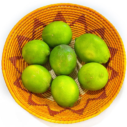 Vibrant handwoven Tucuma palm bowl, filled with fresh limes, showcasing the bowl's capacity and intricate orange and brown pattern