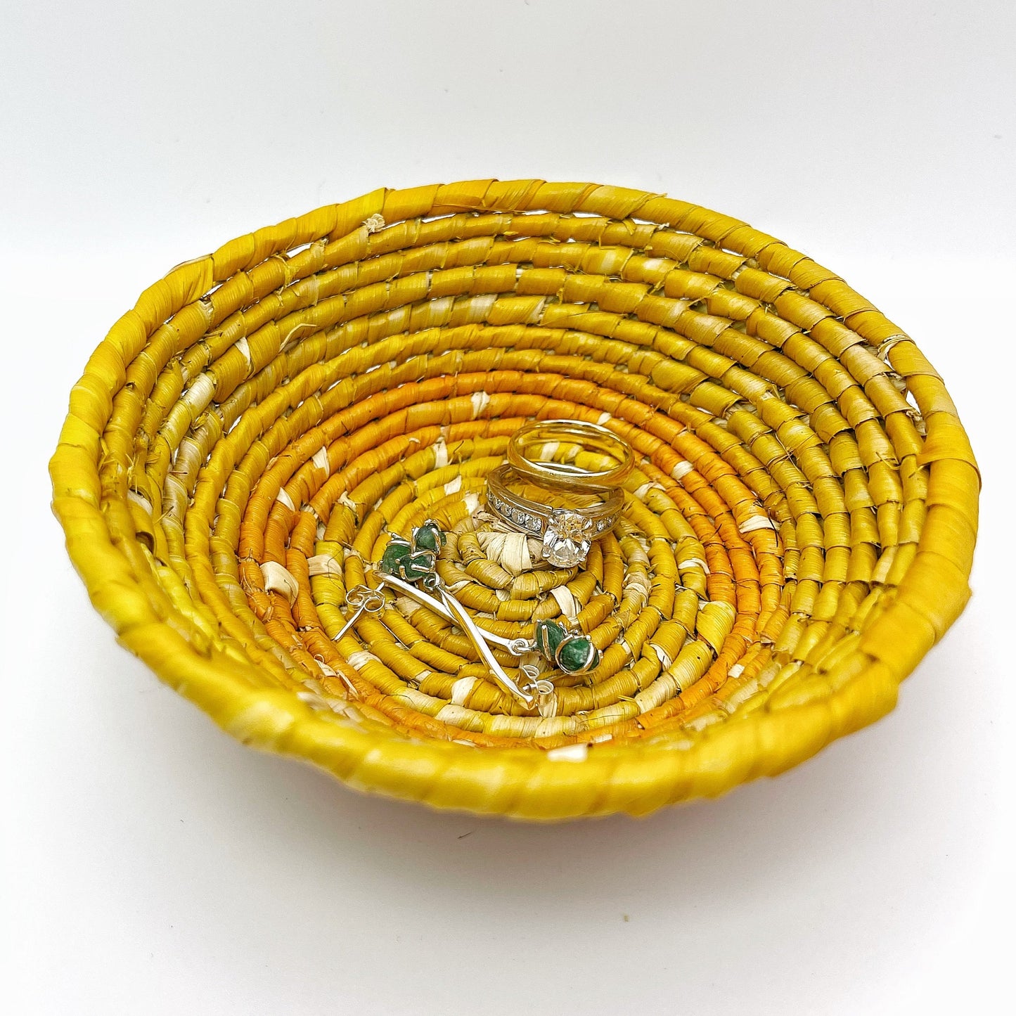  The bowl features a beige center with spiraling patterns in shades of yellow and a bold orange edge, holding earrings and rings, demonstrating its use for small items.