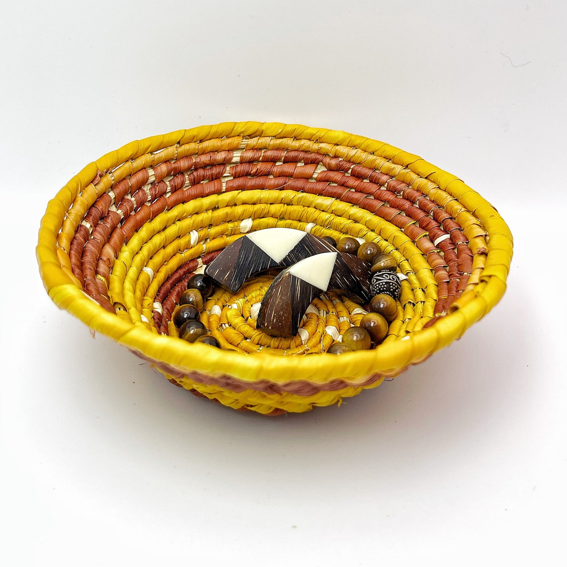 The bowl has a bright yellow rim and interior that transitions to orange and then to a reddish hue, containing beads and jewelry, showing it's suited for holding small items.