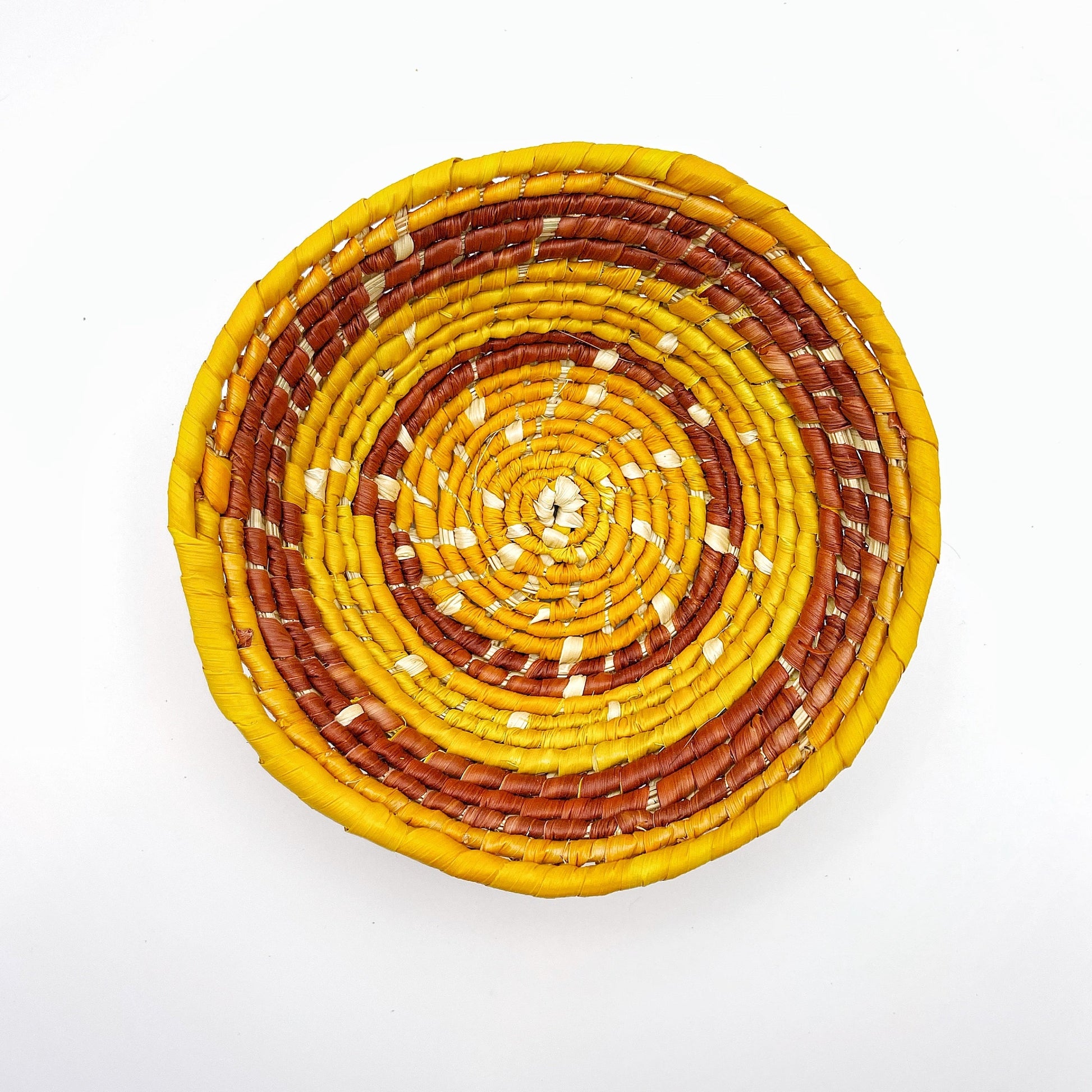 The bowl has a swirling pattern of natural beige, yellow, and reddish-brown colors, demonstrating the intricate handwoven technique used to create it.