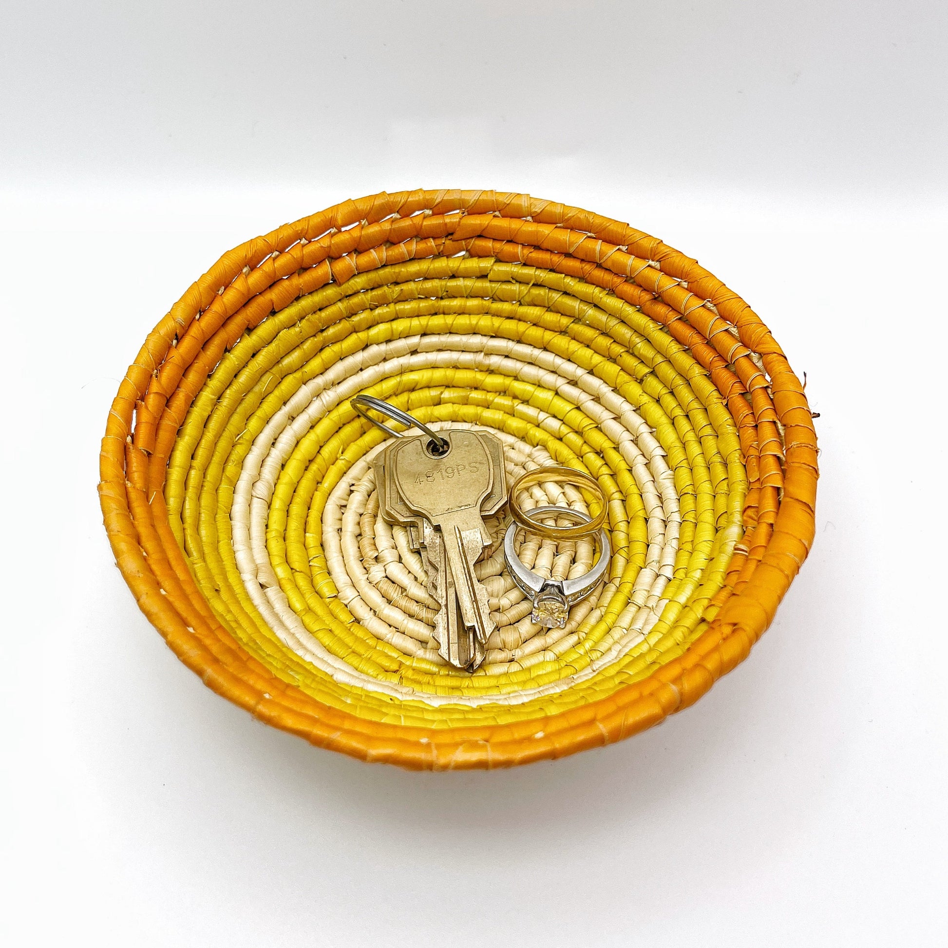 The bowl features a beige center that transitions to yellow and culminates in an orange rim. It contains keys and rings, illustrating its use for storing small items.