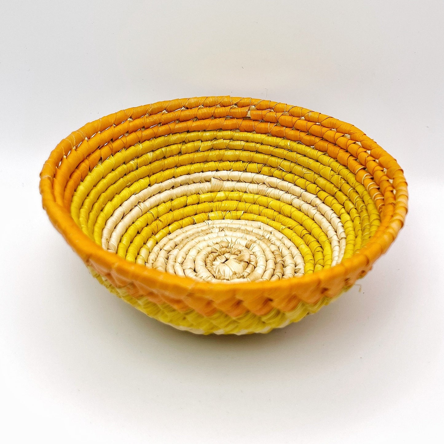 Handwoven Amazonian trinket bowl with a vibrant color gradient. Beige transitions to yellow and culminates in an orange rim. Intricate geometric pattern adorns the bowl's exterior. Made from tucuma palm fibers.