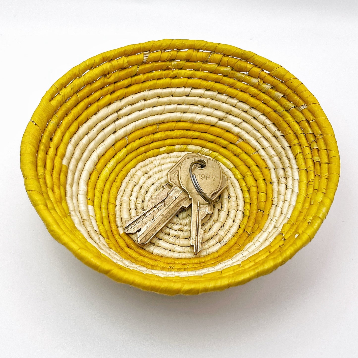 Handwoven Amazonian trinket bowl: natural cream interior, vibrant yellow rim, and intricate coil pattern. Made from tucuma palm fibers, the key feature in the showcased image is its storage capacity for small items.