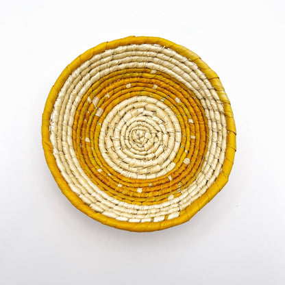 The trinket bowl is handwoven with a natural cream interior and a vibrant yellow rim, showcasing the intricate coil pattern characteristic of tucuma palm craftsmanship.