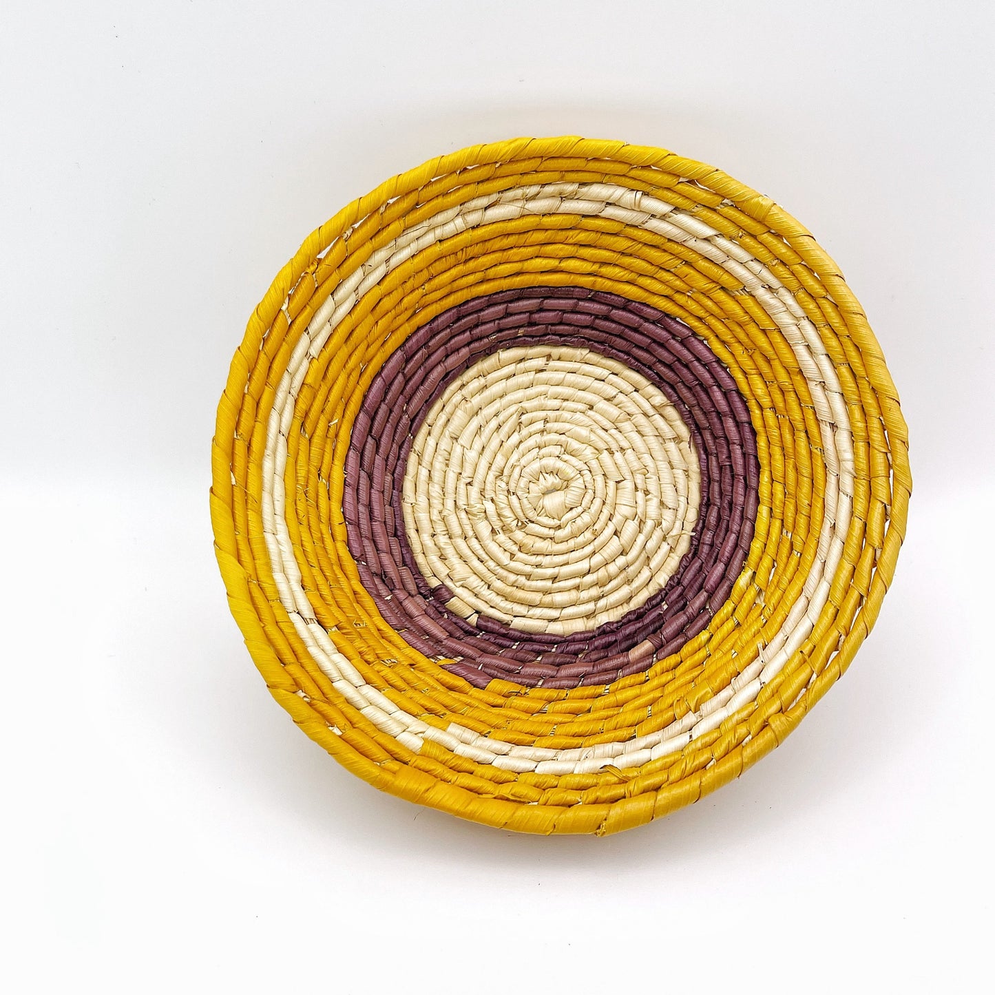 A Trinket bowl displays a spiral pattern, starting with a natural beige center, followed by concentric circles of burgundy, white, mustard yellow, and outermost deep yellow.