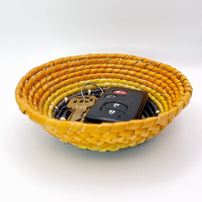 The bowl showcases a pattern of spiraling hues from light beige to yellow and rich orange, filled with keys and a car remote to display its practical use for small objects.