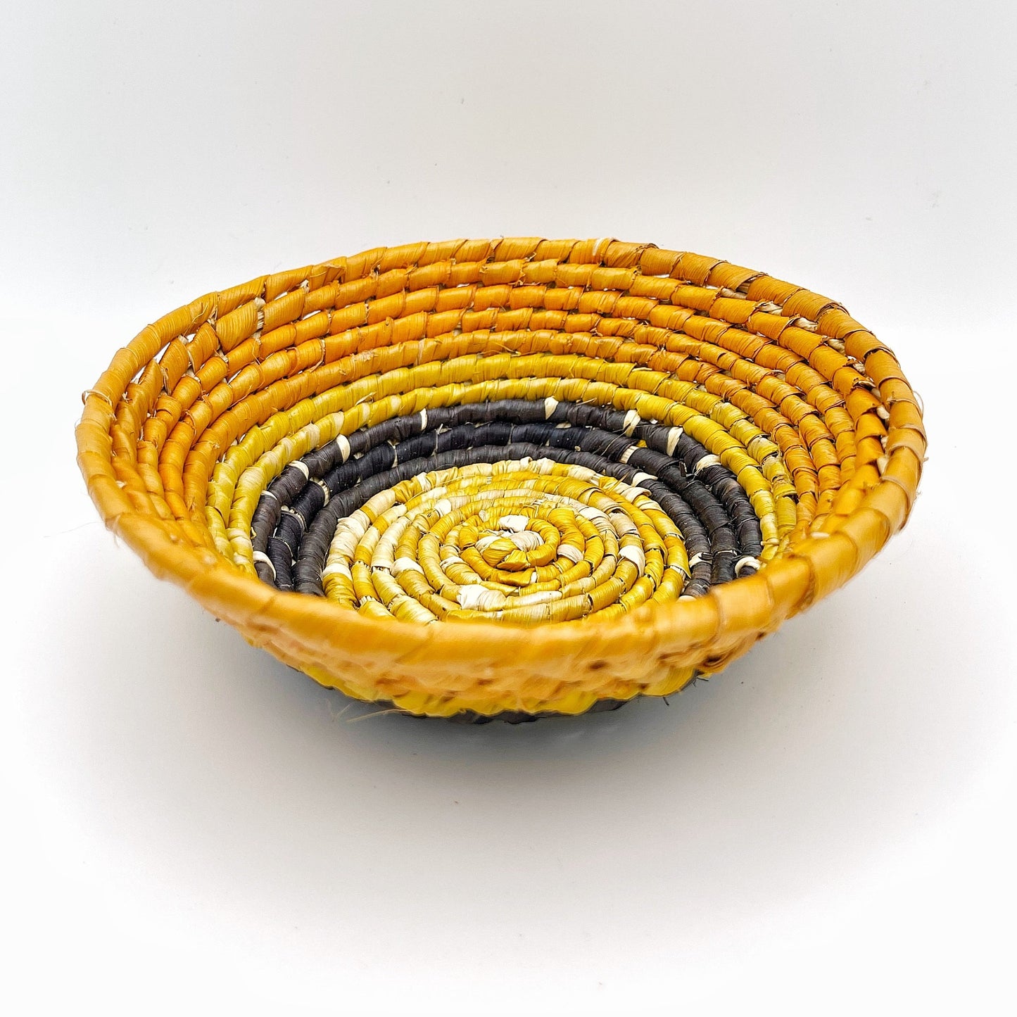 The trinket bowl exhibits a vibrant yellow outer ring with an inward gradient to darker tones, and a light beige center, all in a coiled pattern. It’s designed to hold small items such as jewelry.