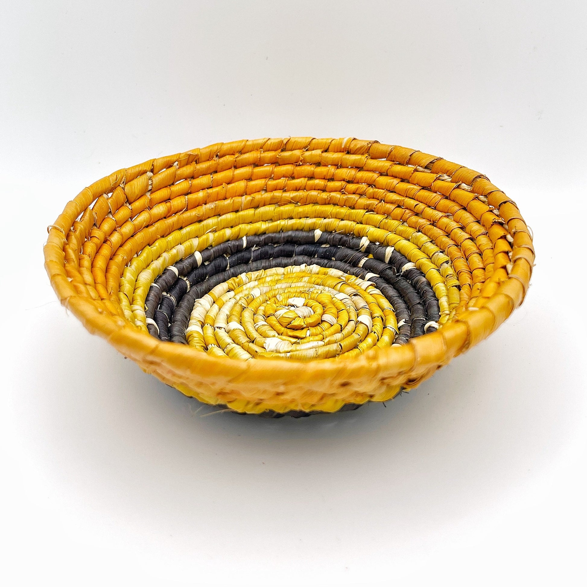 The trinket bowl exhibits a vibrant yellow outer ring with an inward gradient to darker tones, and a light beige center, all in a coiled pattern. It’s designed to hold small items such as jewelry.