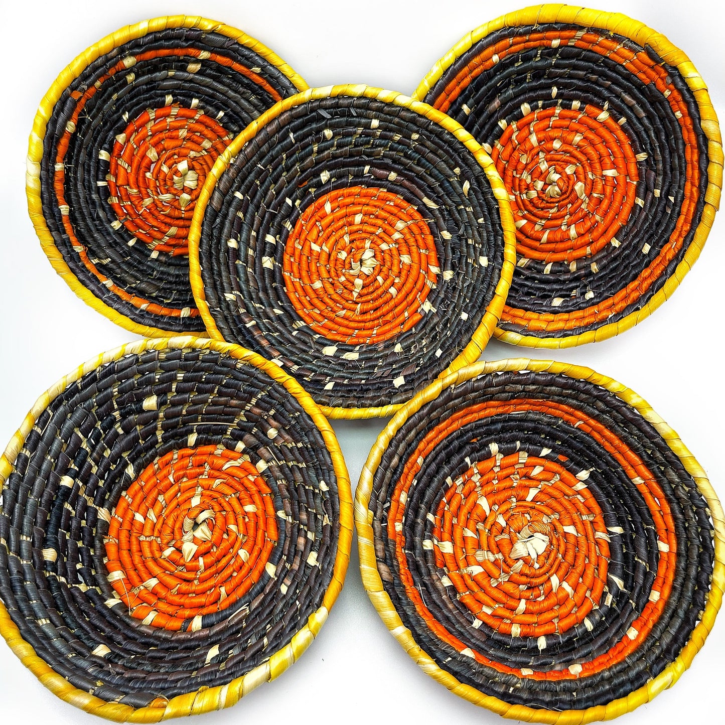 Five trinket bowls feature a central spiral of beige, surrounded by concentric circles of orange, black, and vibrant yellow at the edges, highlighting the handwoven craft.