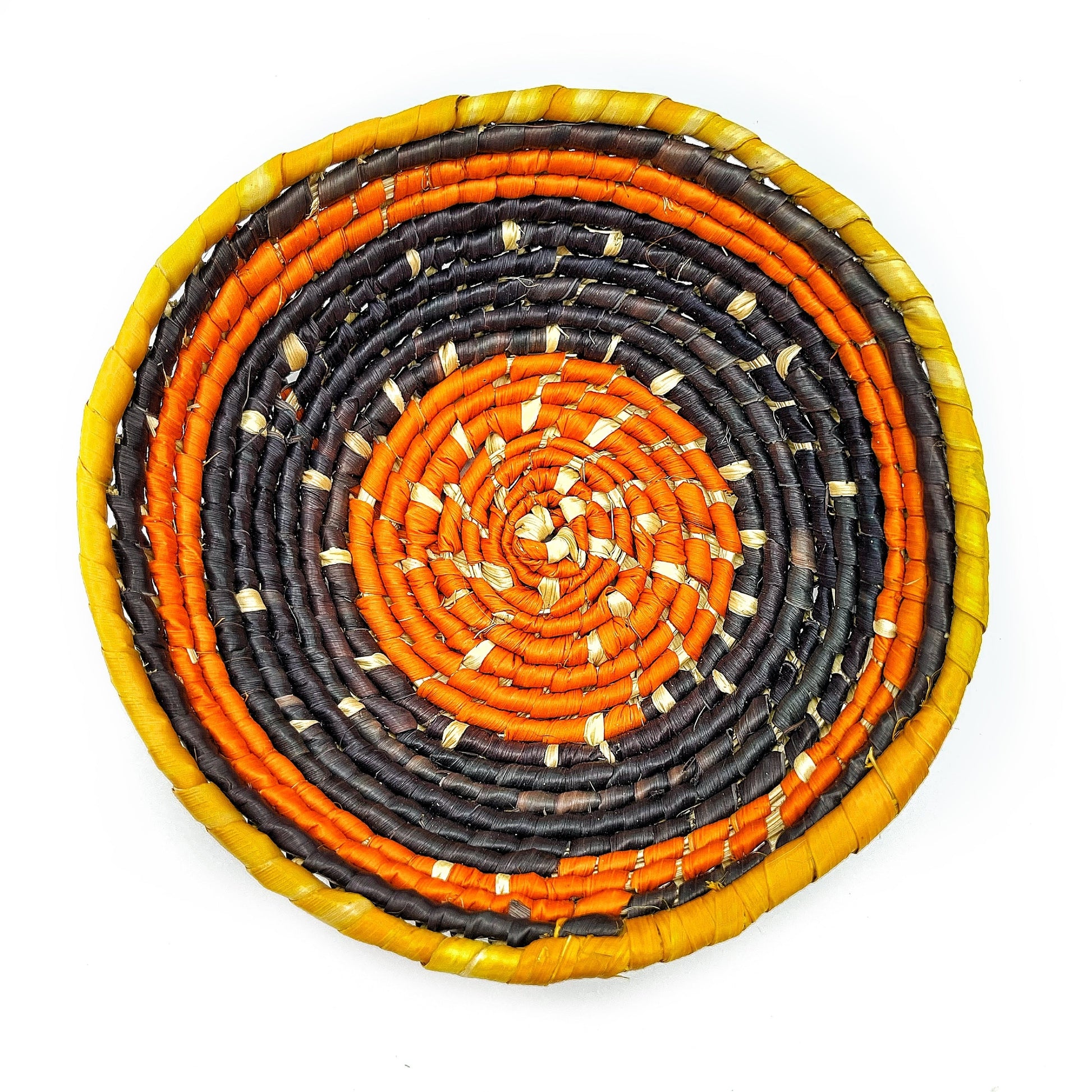 The woven bowl features a dynamic color palette with concentric circles of beige, fiery orange, and deep black, edged with a bold yellow rim, creating a striking spiral pattern.