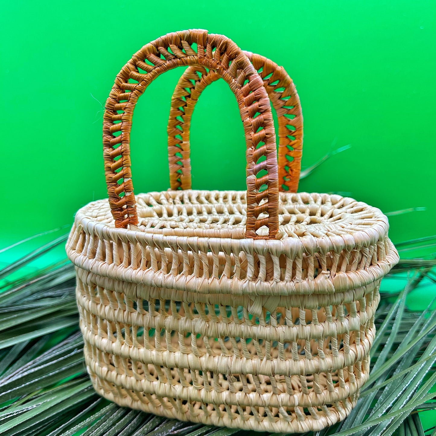 Handwoven tucuma palm basket: sturdy double handle, cylindrical shape. Natural beige color showcases woven texture; handles wrapped in earthy brown with hints of green