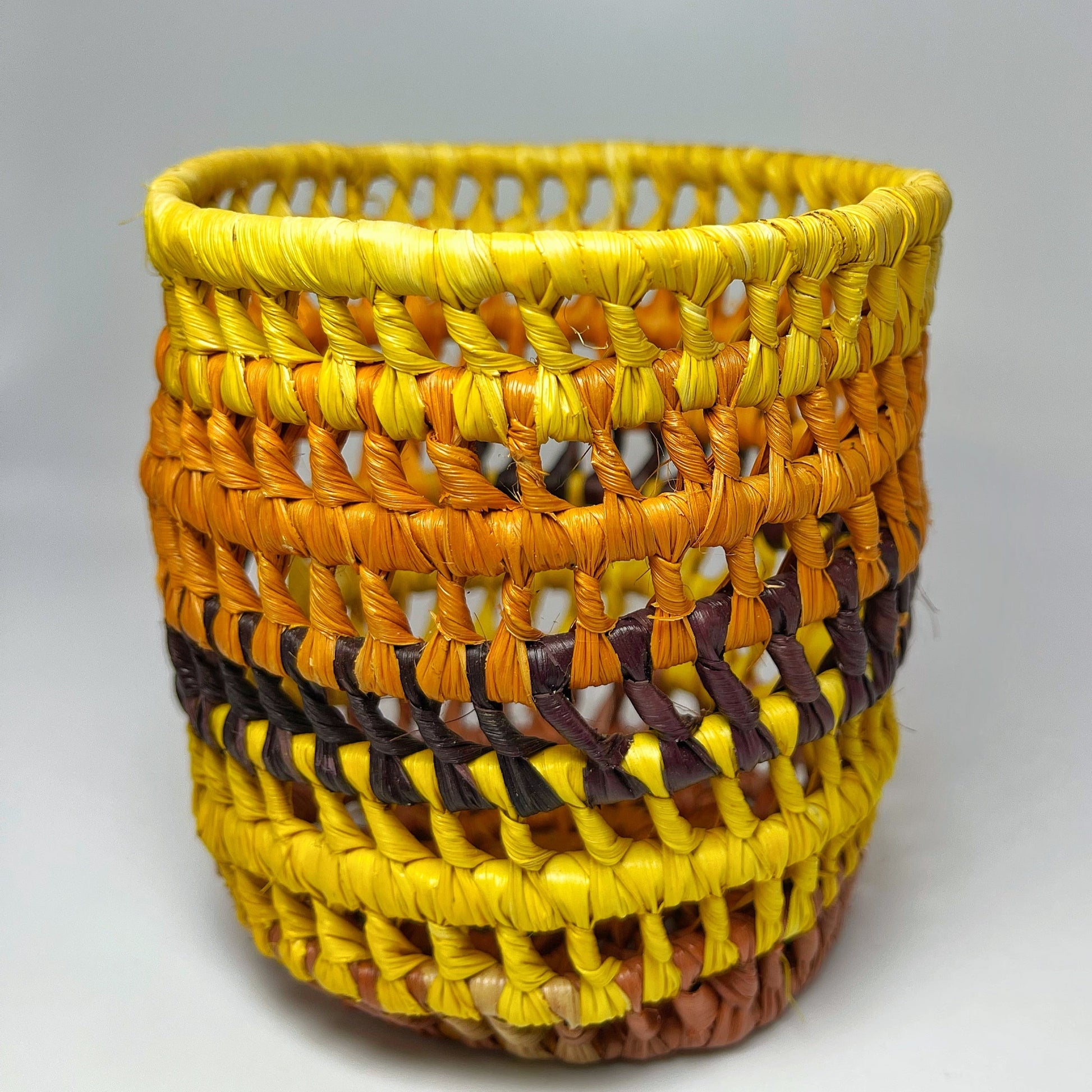 A handwoven holder featuring a yellow openwork top, transitioning to orange, purple, and brown hues with a solid base.