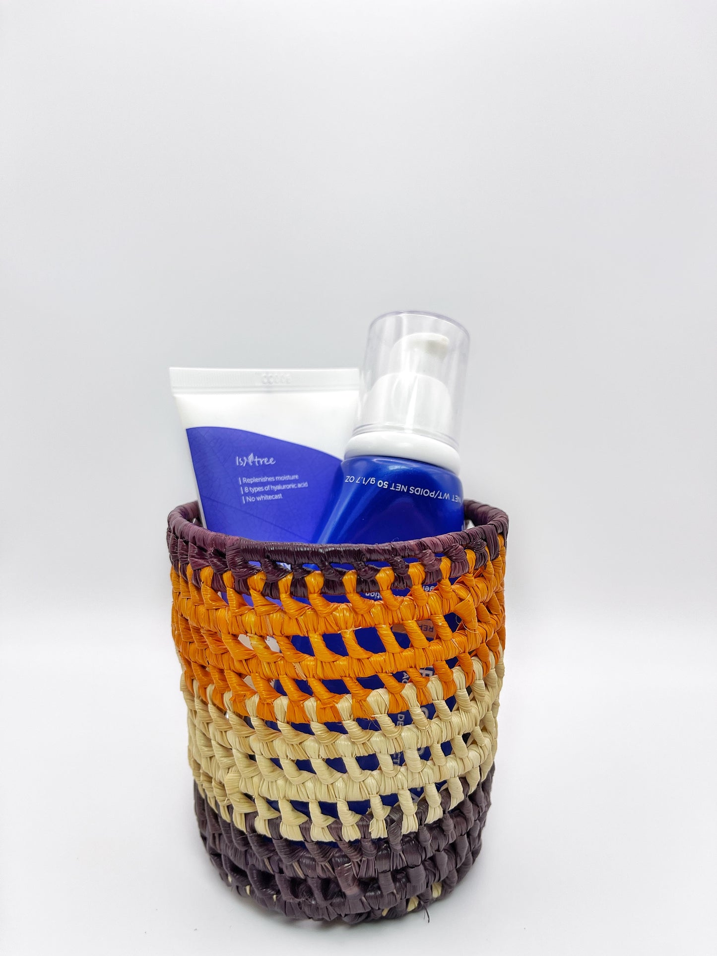 A handwoven holder in purple, orange, and cream, containing skincare products, illustrating its practical use.