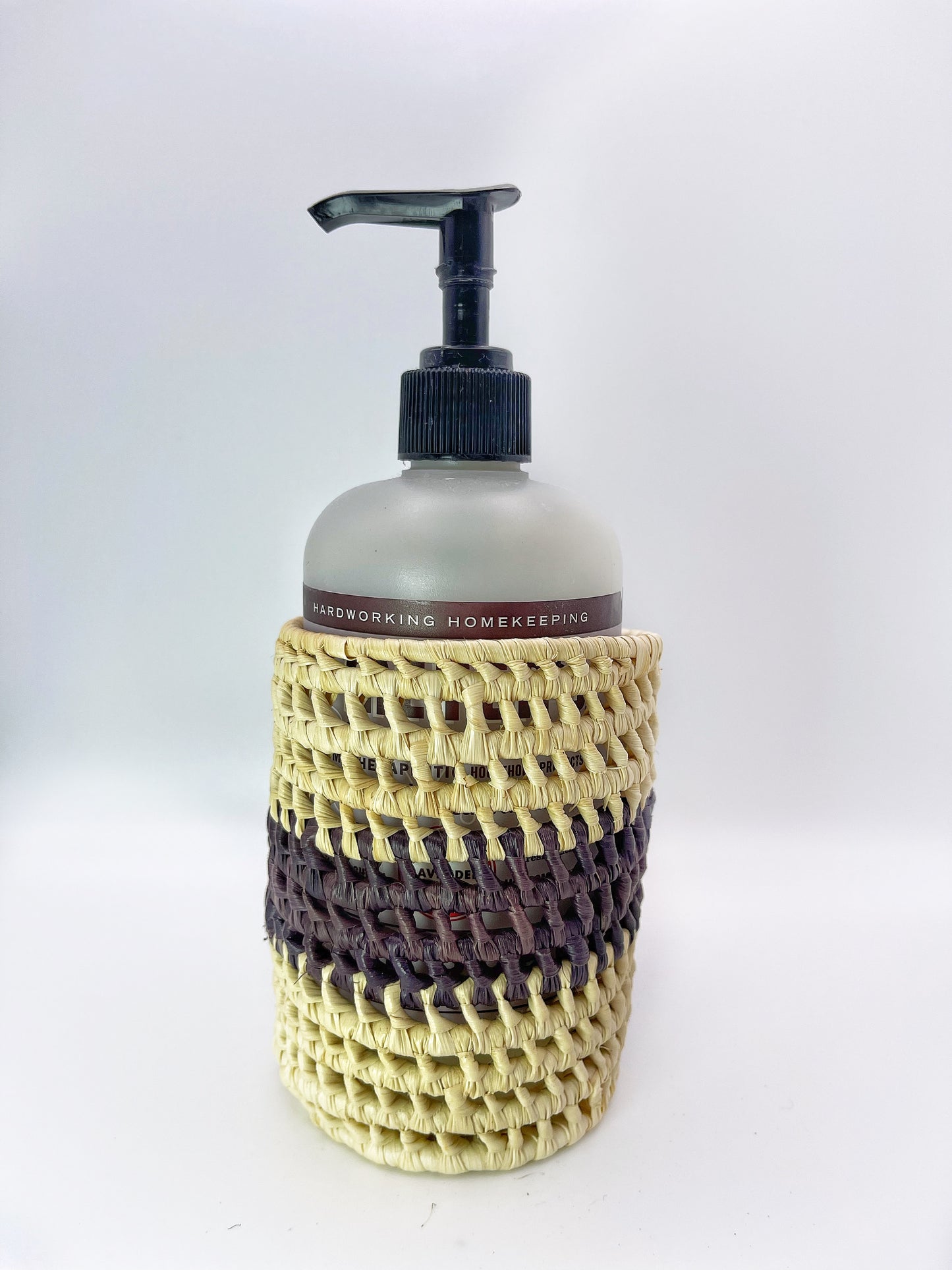 A cream and purple woven holder with an open top, cradling a dispenser bottle, demonstrates the holder's functional design.