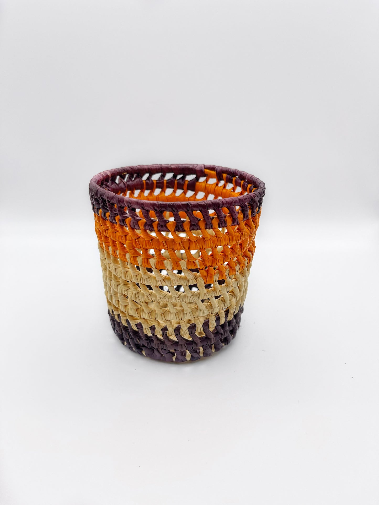 An openwork handwoven holder with cream, orange, and purple bands, displaying a blend of function and style.