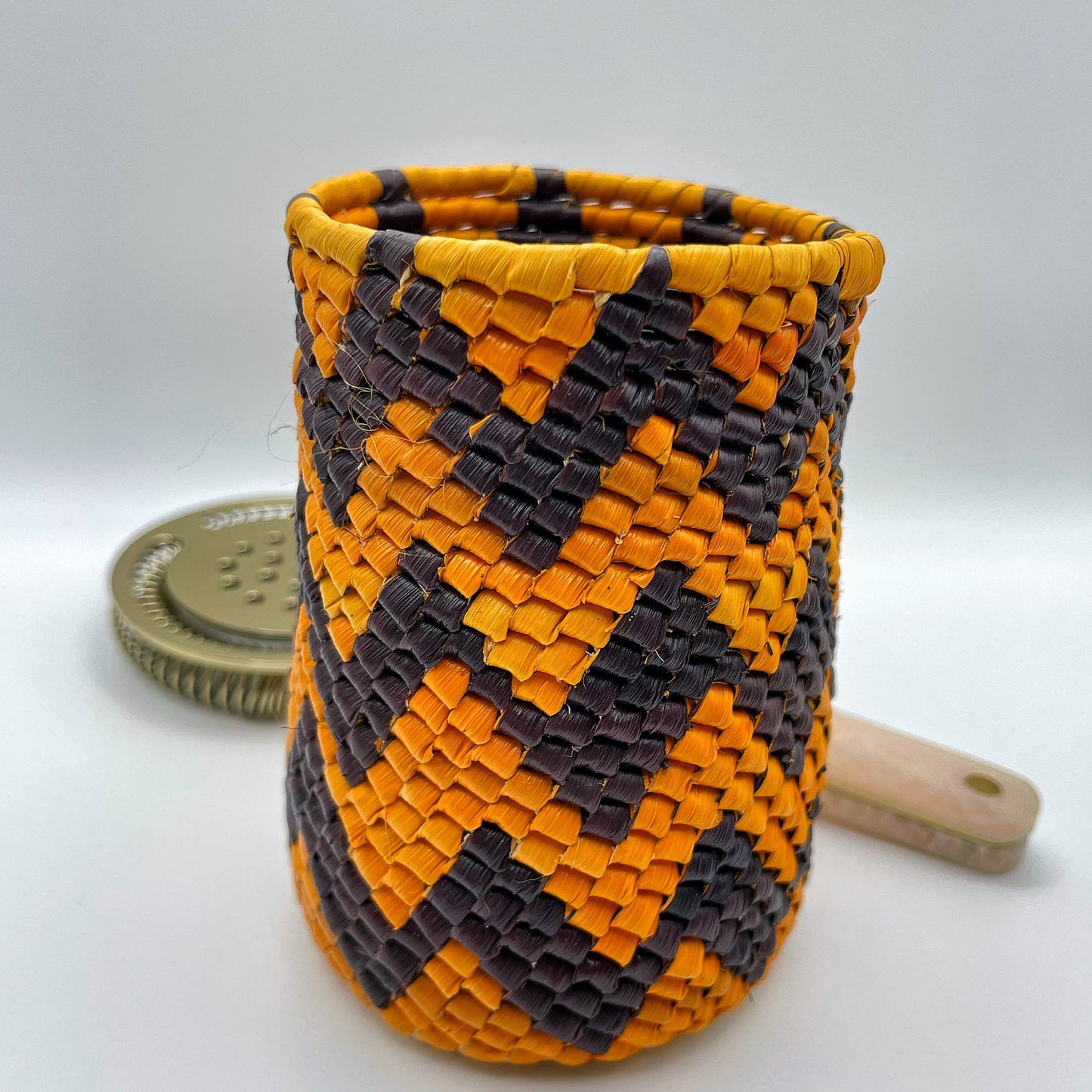 Handwoven holder with a diagonal chevron pattern in orange and black, featuring a tight weave and sturdy rim.