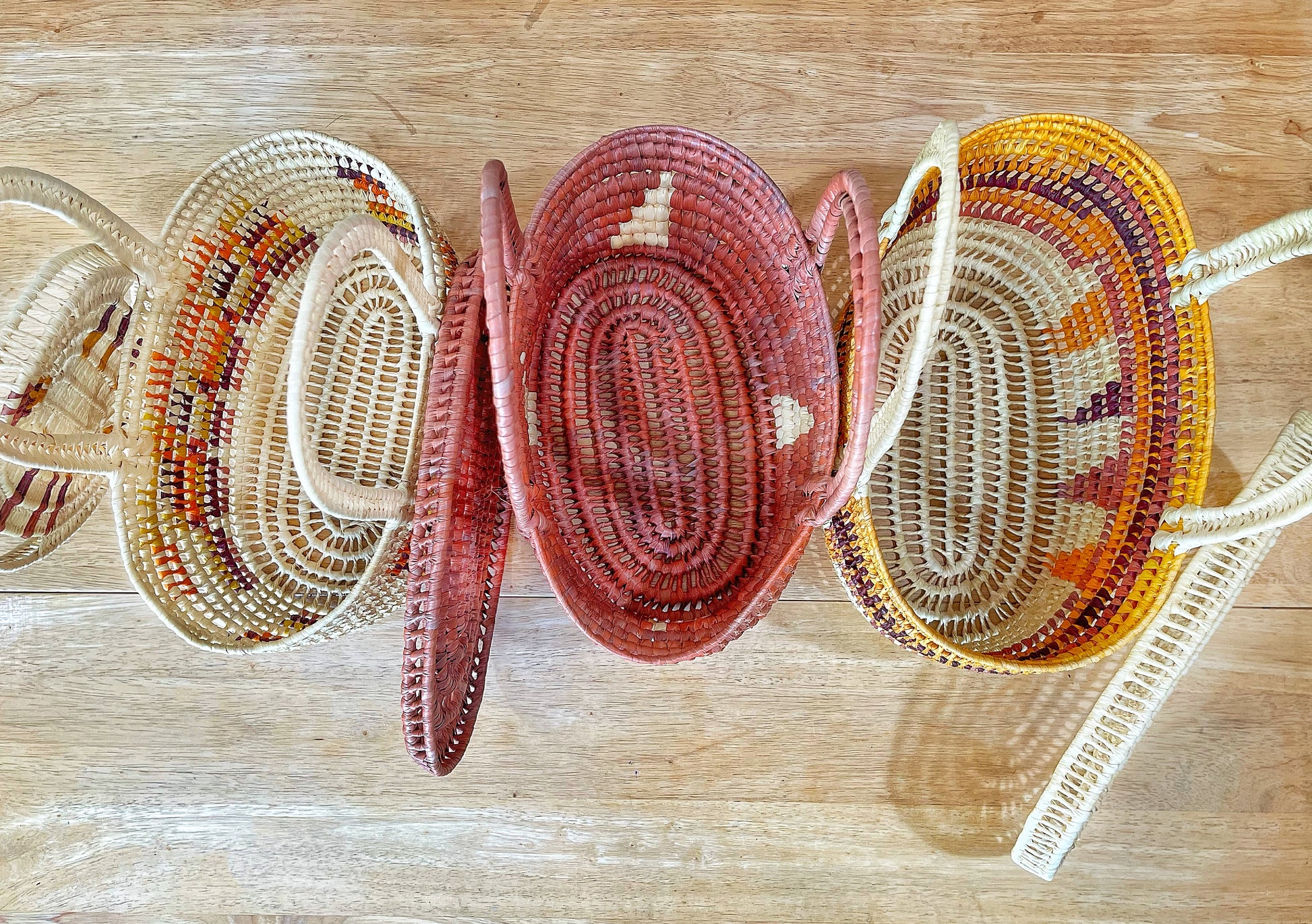 Three Tucuma fiber baskets from Brazil are displayed with lids open. The left is cream with earth-toned patterns; the center in terracotta; the right mixes yellows, oranges, and reds. All exhibit intricate concentric designs, showcasing the roomy interiors and expert weaving.