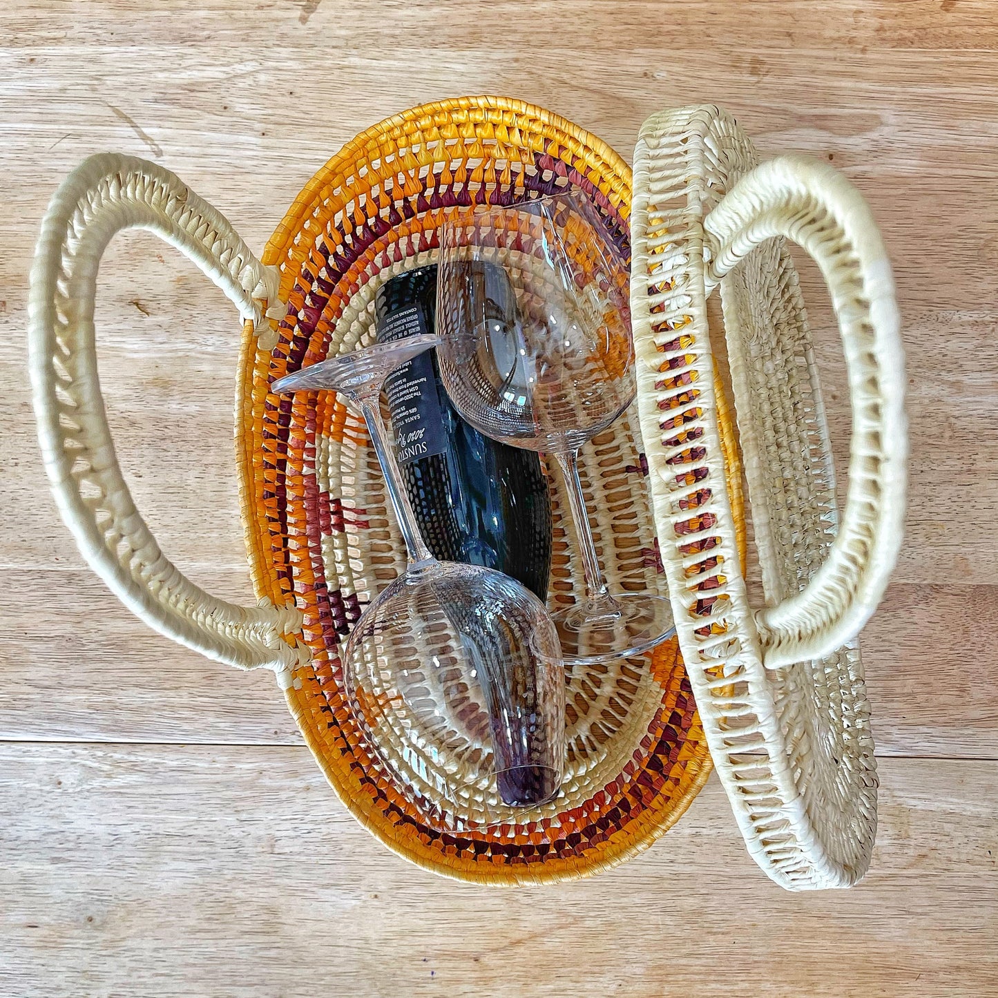  Overhead view of two woven baskets: one natural cream, the other a gradient from yellow to burgundy. A pair of sunglasses rests inside, contrasting modernity with tradition against a wooden backdrop.