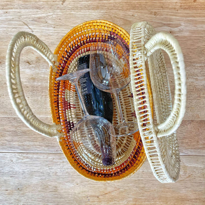  Overhead view of two woven baskets: one natural cream, the other a gradient from yellow to burgundy. A pair of sunglasses rests inside, contrasting modernity with tradition against a wooden backdrop.