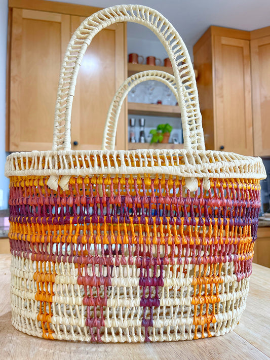  A handwoven basket with a cream base and vibrant stripes of orange, yellow, and burgundy stands out in a warm kitchen setting.