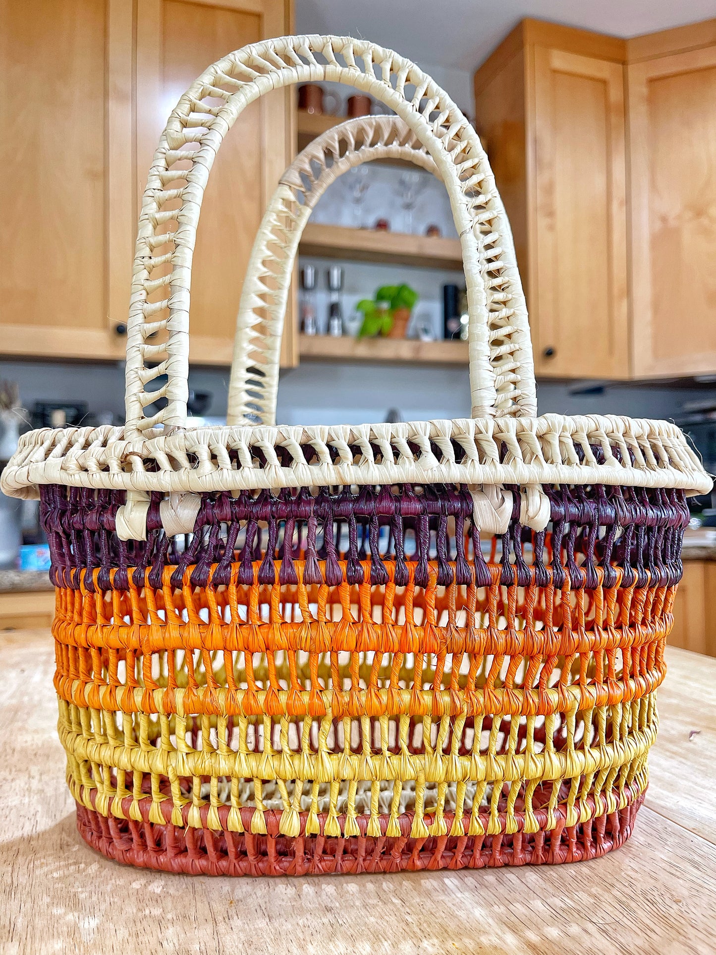 Vibrantly woven Tucuma palm basket, featuring a spectrum from yellow to orange to deep brown, with cream accents and a detailed, sturdy handle