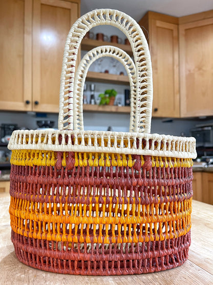 Robust handwoven Tucuma palm basket with vibrant layers of red, orange, and yellow, contrasted by a cream handle, displaying the intricate craftsmanship