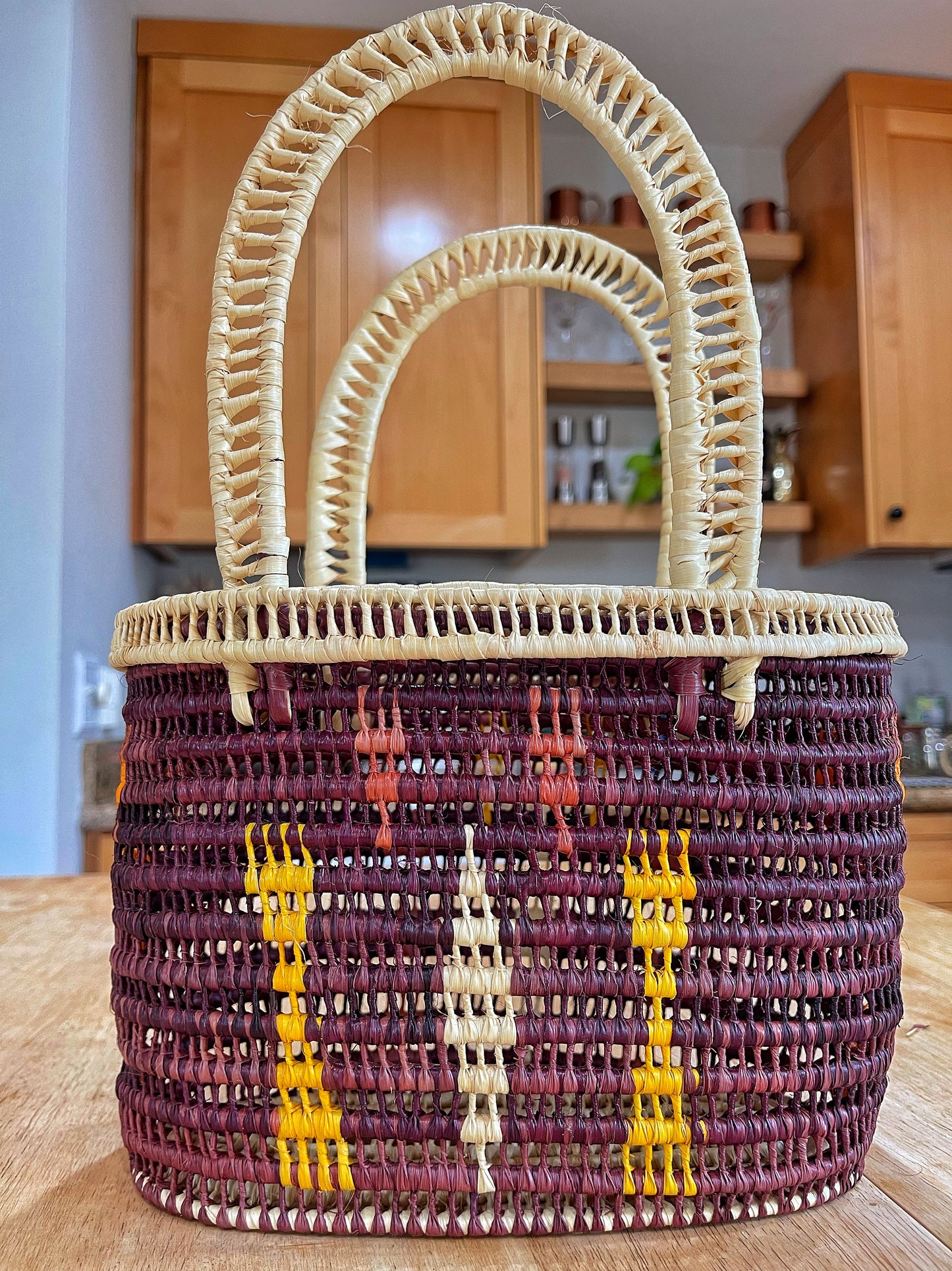 Sturdy handcrafted basket with a natural cream rim and handles, woven with deep purple Tucuma palm fibers, and detailed with orange and yellow vertical stripe patterns