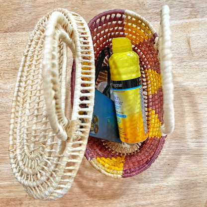 A small, open-lidded handwoven Tucuma palm basket from Brazil, sized 9x6x6 inches, displays its utility by holding a phone, sunglasses, and sunscreen, showcasing the basket's practicality and artisanal beauty