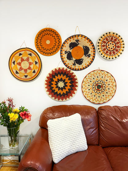  A cozy room with a leather couch, adorned with a white cushion, and a wall above decorated with colorful mandala wall art, plus a glass vase of bright flowers.