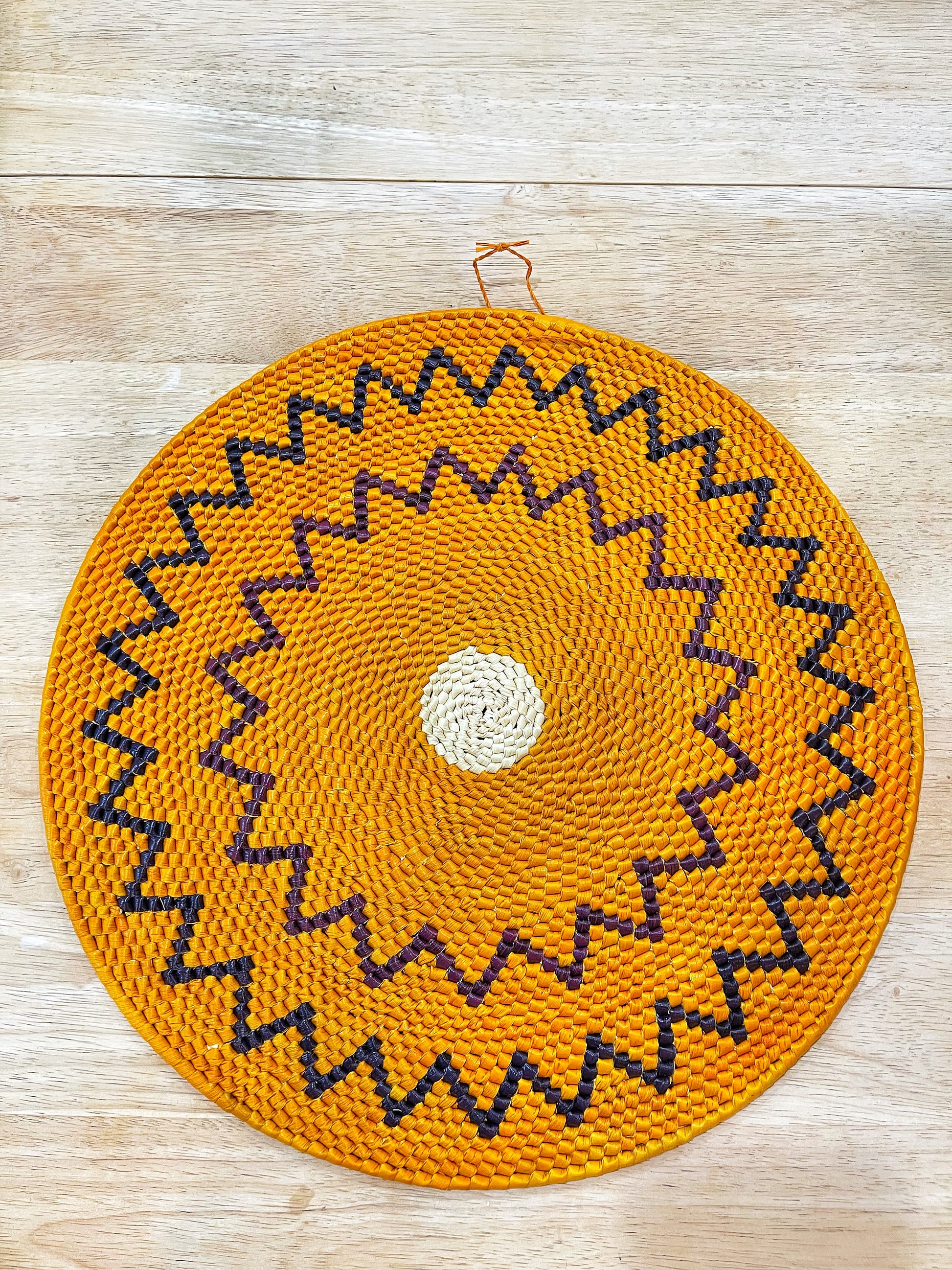 This vibrant mandala wall art showcases a vivid orange backdrop with concentric patterns of jagged black and purple zigzag lines, culminating in a central cream-colored circle. It exudes a lively, energetic aura.