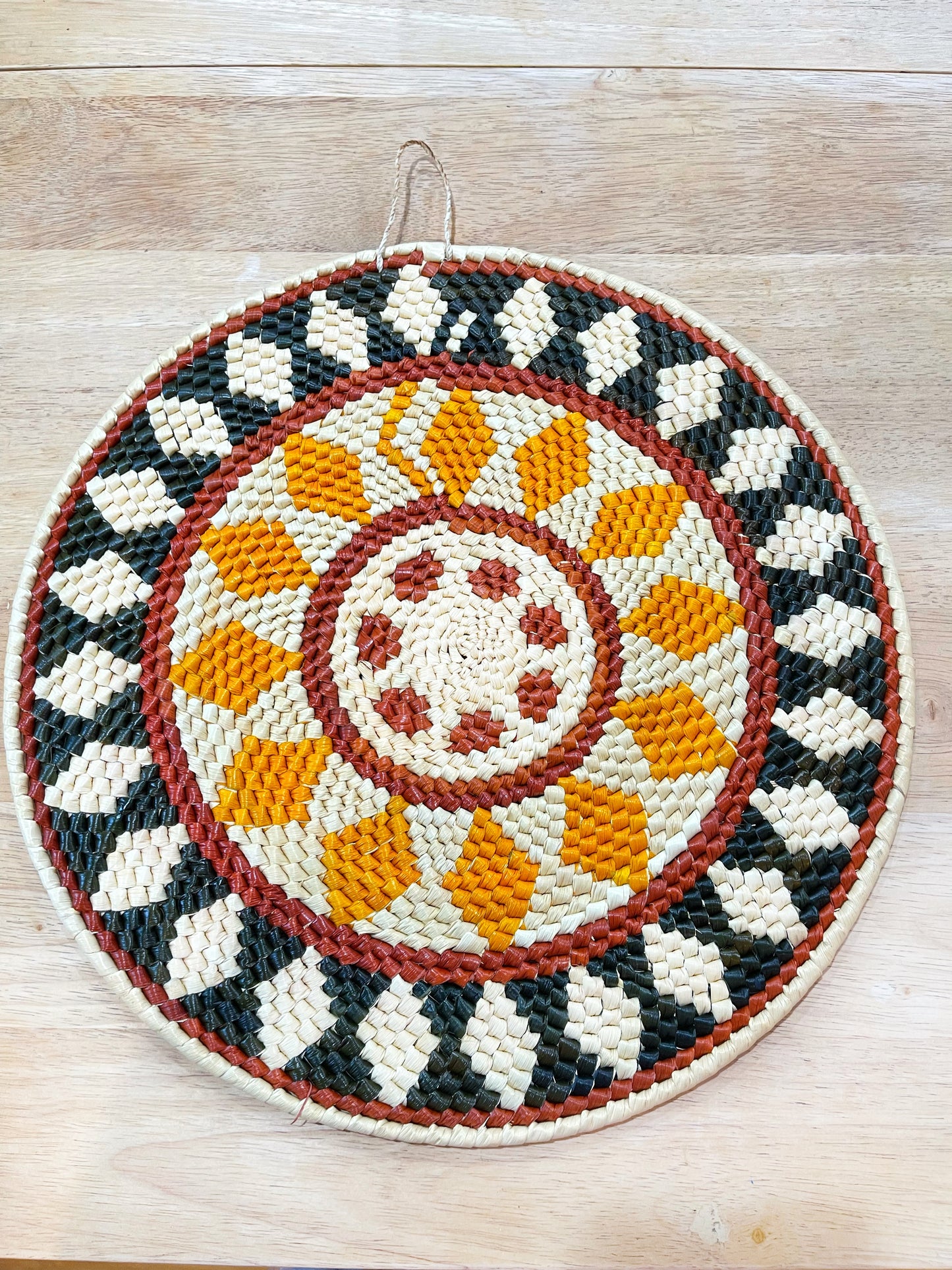 This woven mandala art piece displays a captivating geometric pattern in a rich palette of cream, orange, yellow, brown, and black, creating an intricate mosaic of angular and circular forms encircled by a bold russet border.