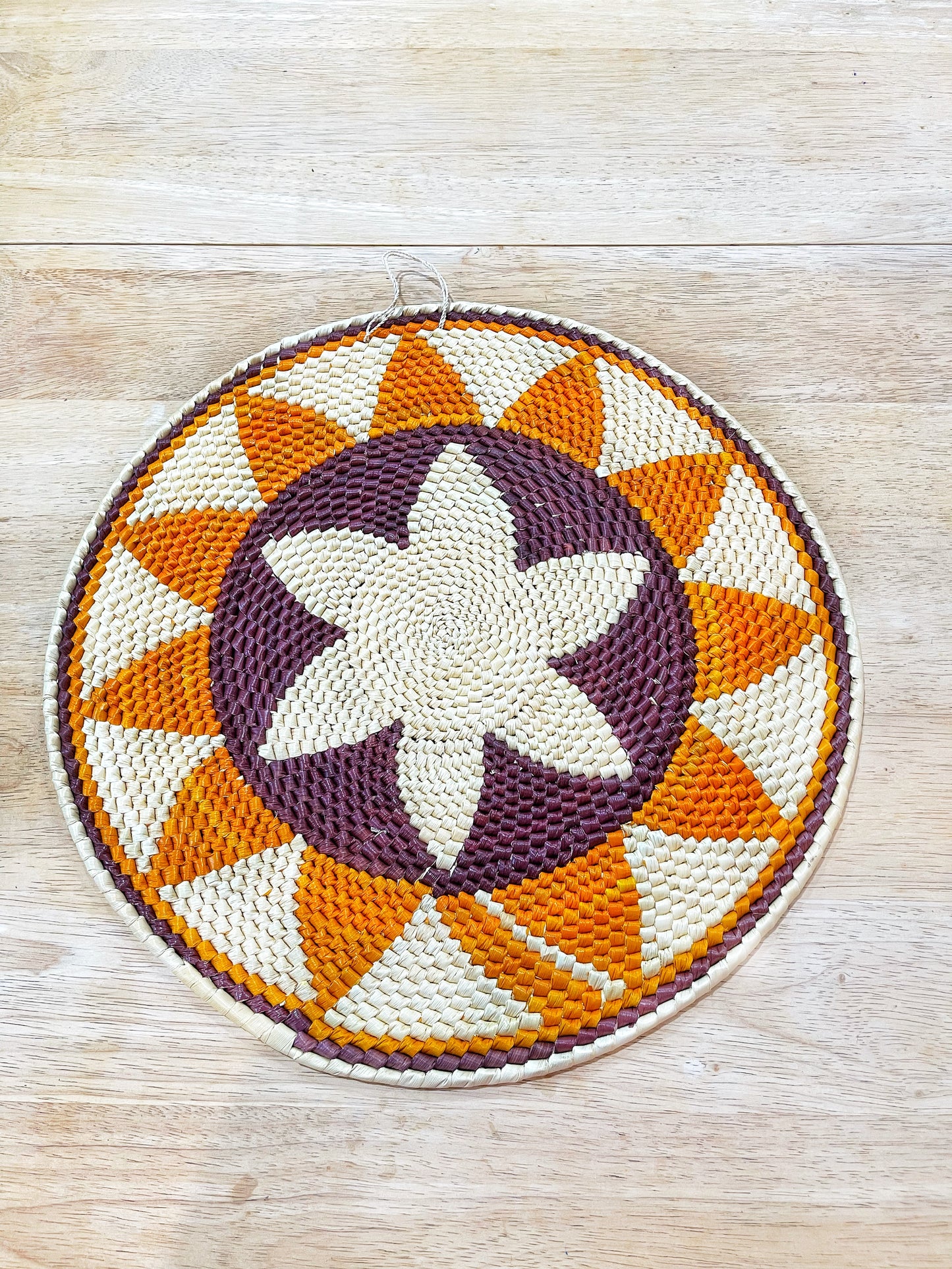 This handcrafted mandala showcases a central starburst pattern in shades of cream and deep purple, framed by a series of orange and cream triangles creating a dynamic contrast, all encircled by a neat cream edge.