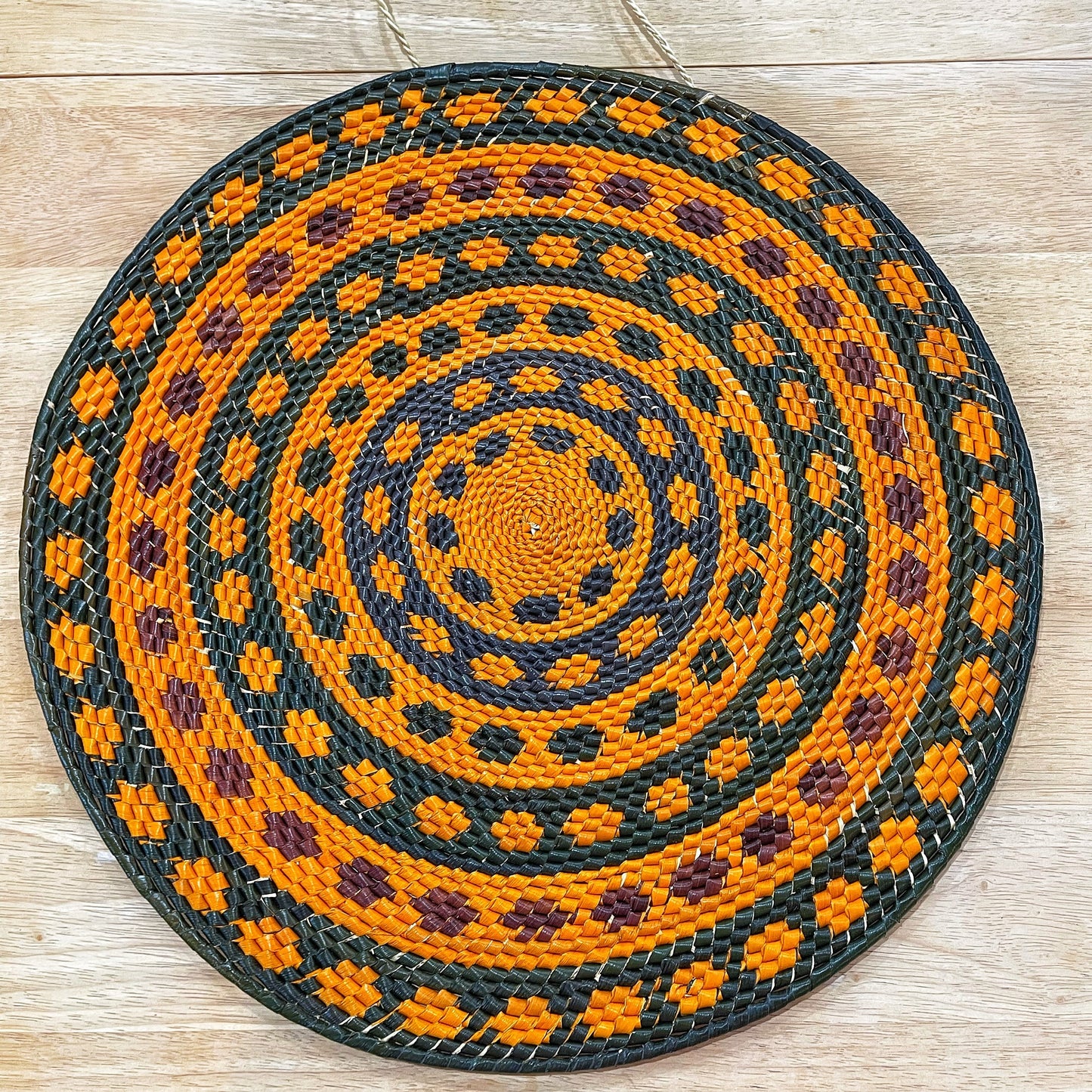 Artisanal mandala wall art, handwoven with a vibrant orange, dark green, blue, purple  and brown pattern, radiating from the center in concentric circles.