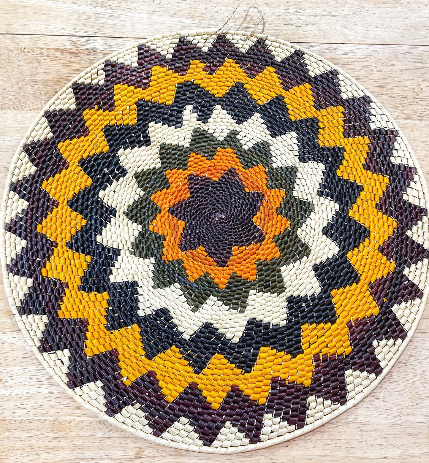 This handwoven wall mandala features an intricate pattern in orange, green, cream, purple, yellow and blue, adding a warm, artisanal touch to any room.