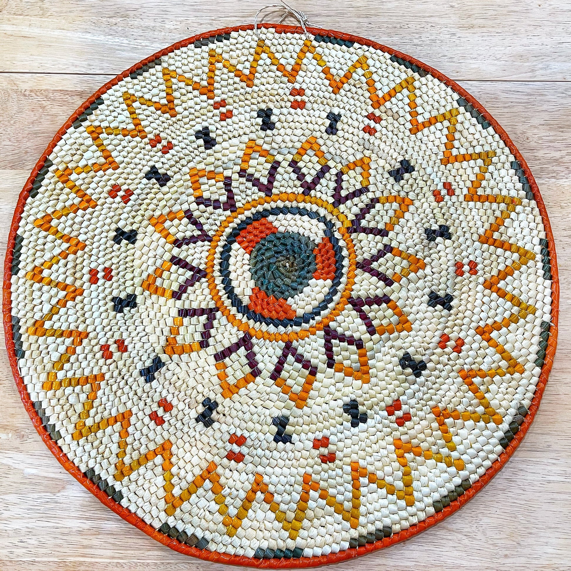 Handwoven mandala wall decor in shades of green, red, orange, yellow, and purple. The mandala features a geometric flower pattern with intricate details.