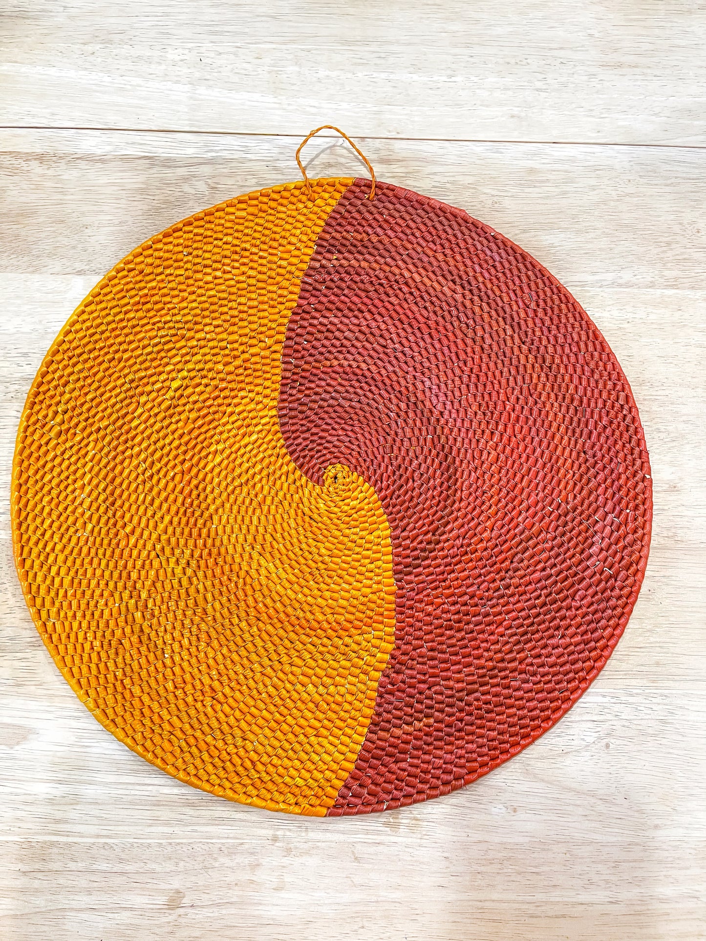 This mandala wall piece presents a yin-yang design, with a warm golden yellow on one side and a rich terracotta red on the other, both featuring intricate woven textures.